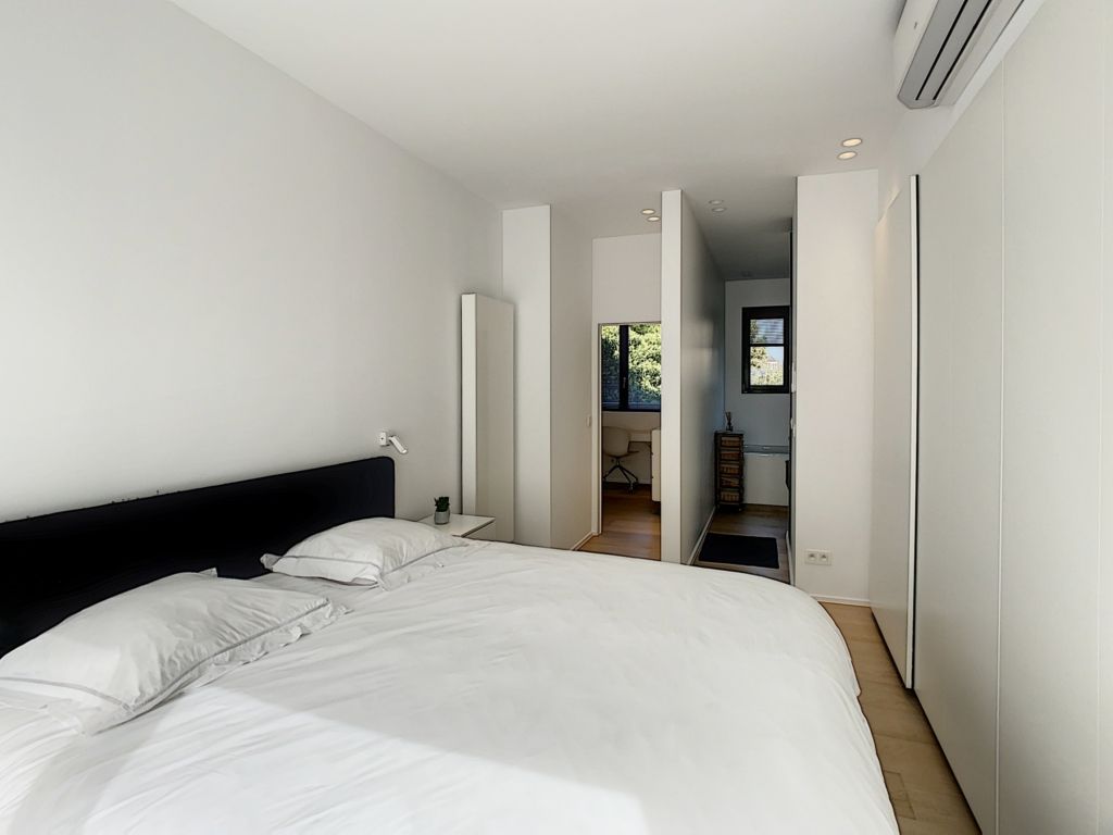 Chambre minimaliste moderne avec literie blanche, lumière naturelle et vue sur la nature extérieure.