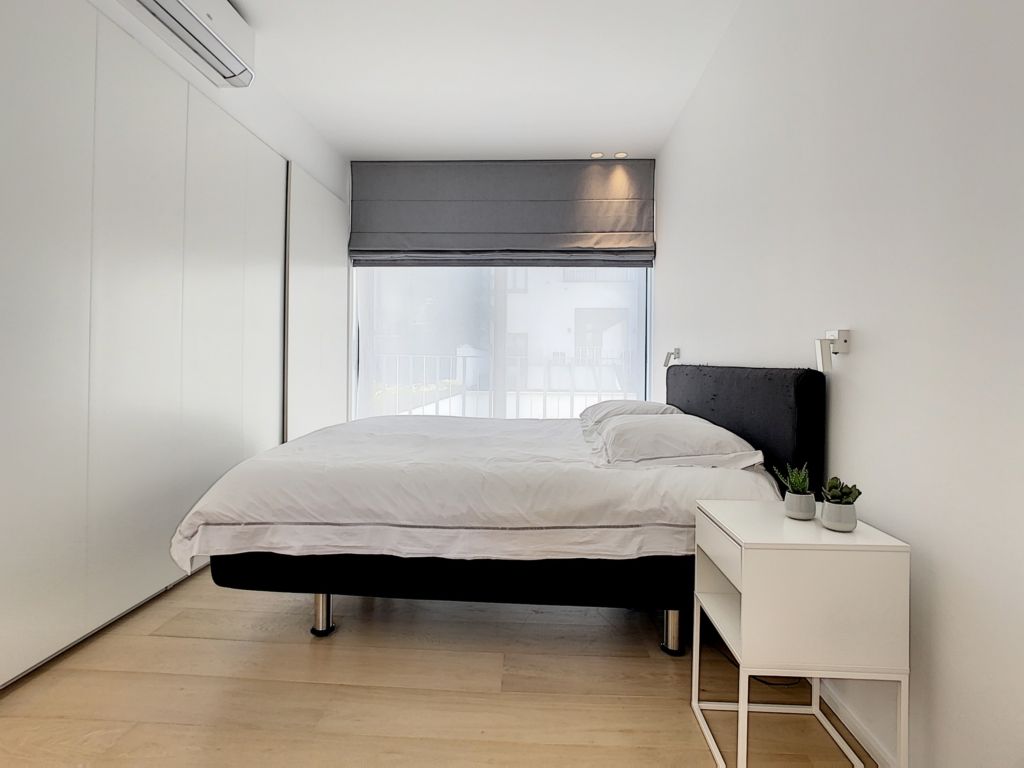 Chambre minimaliste avec lit noir, plantes vertes, mur blanc et lumière douce.