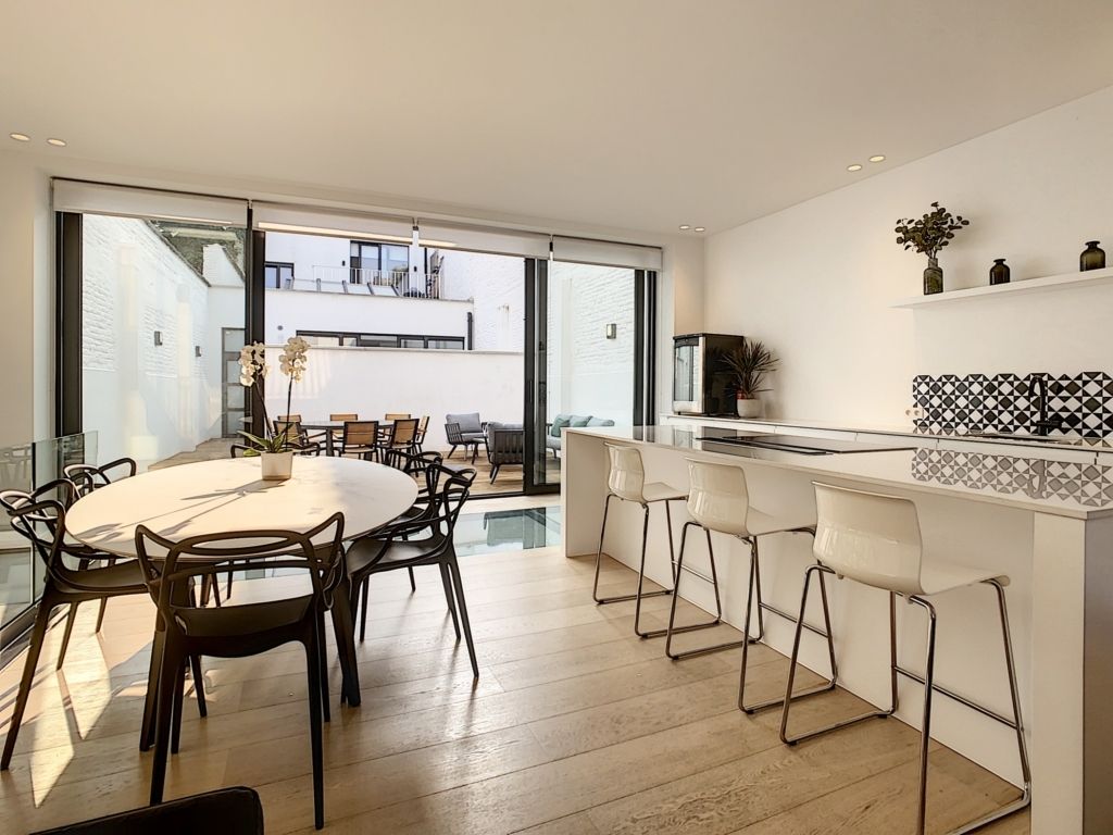 Cuisine moderne ouverte, lumineuse et minimaliste avec coin repas, îlot blanc et décoration élégante.