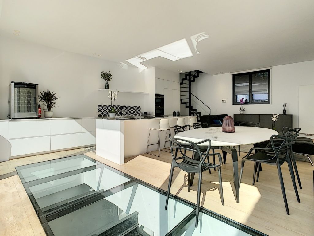 Cuisine moderne lumineuse avec îlot, table ronde en verre et décoration végétale élégante.