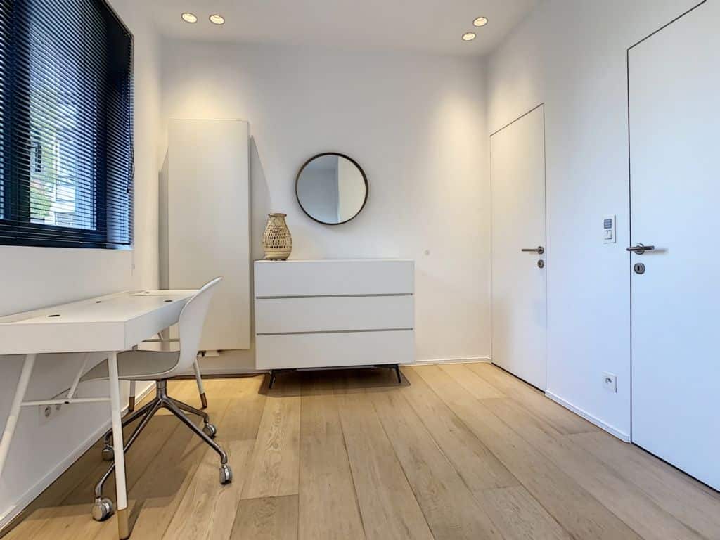 Intérieur moderne minimaliste avec miroir circulaire, bureau épuré et décor blanc lumineux.