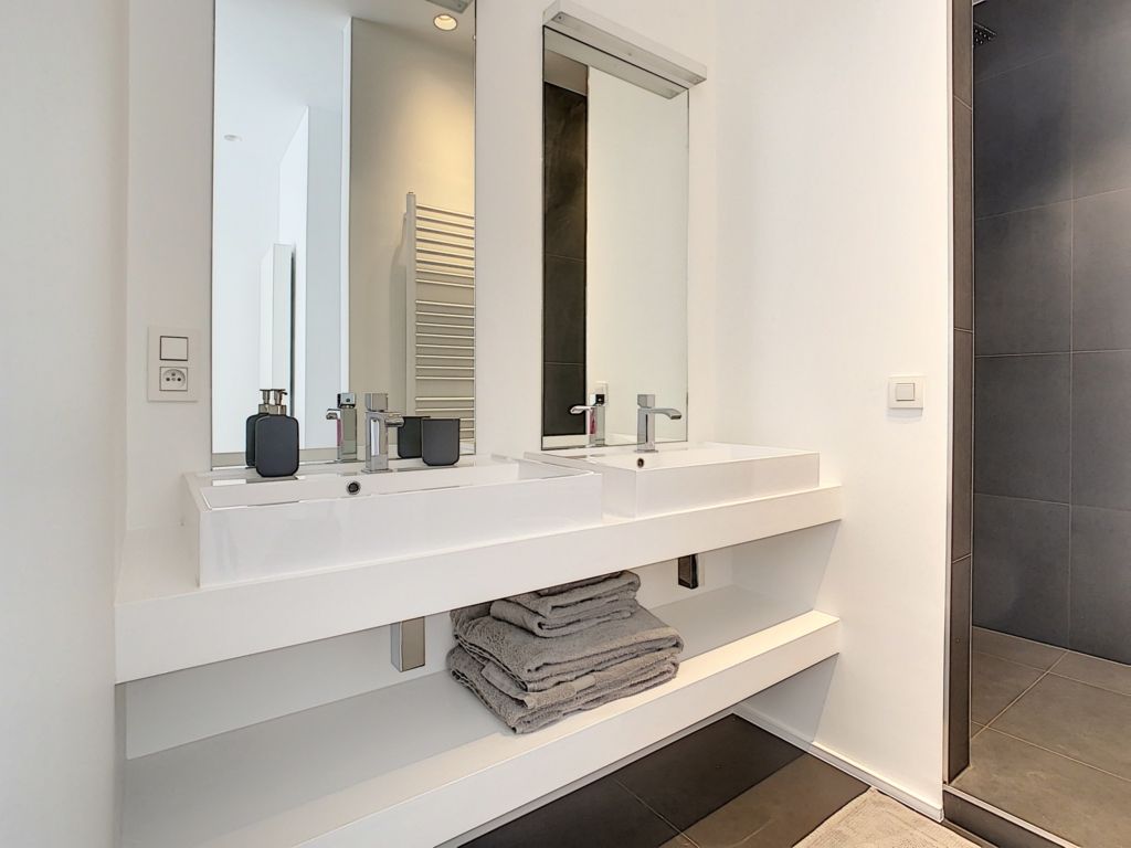 Salle de bain moderne avec double vasque, miroirs rectangulaires, robinetterie chromée, et déco minimaliste.