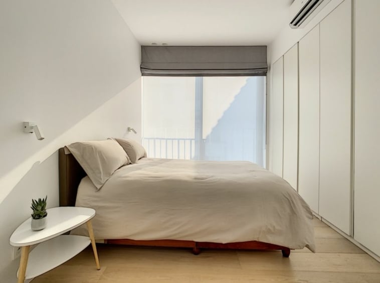 Chambre minimaliste lumineuse avec lit en bois, fenêtre naturelle, placards blancs et touche de verdure.