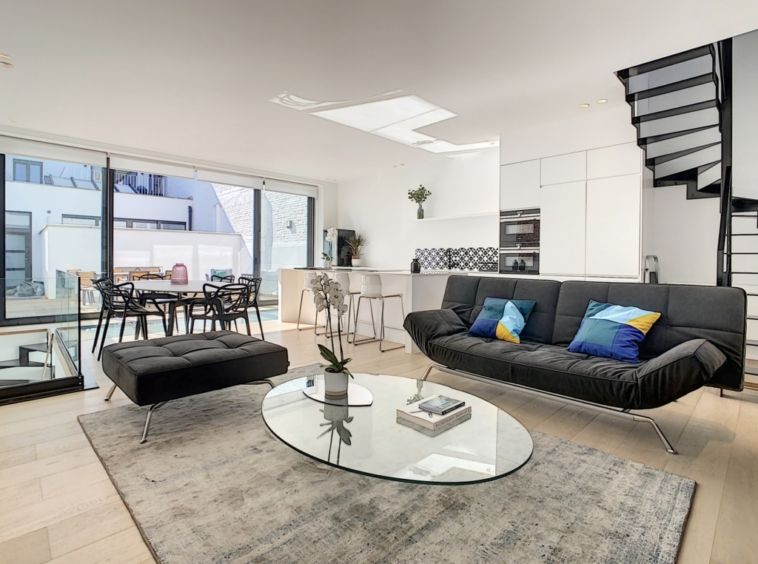Salon moderne lumineux avec canapé, cuisine ouverte blanche et vue sur terrasse élégante.