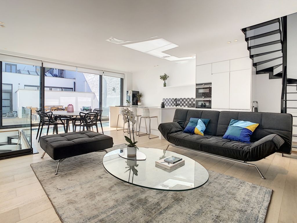 Salon moderne lumineux avec canapé, cuisine ouverte blanche et vue sur terrasse élégante.