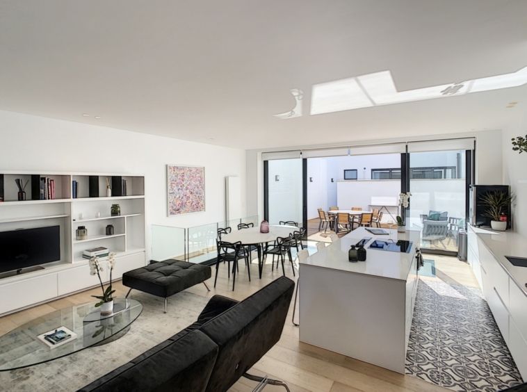 Salon moderne lumineux avec cuisine ouverte, canapé noir, terrasse ensoleillée, espace convivial et élégant.