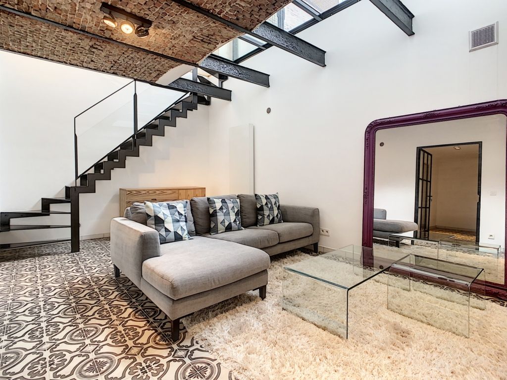 Salon moderne lumineux avec canapé gris, grand miroir violet, escalier minimaliste et décoration élégante.