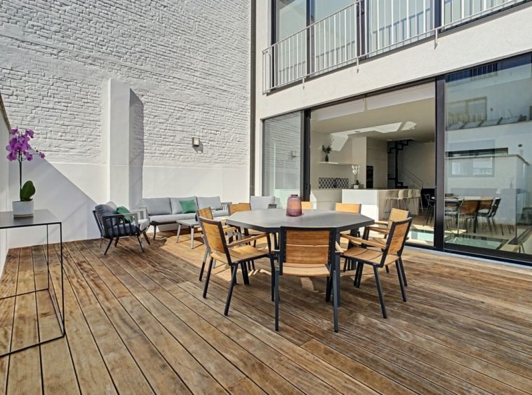 Terrasse moderne en bois avec espace repas, coin détente, lumière naturelle et touches végétales élégantes.