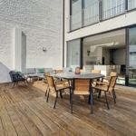 Terrasse moderne élégante avec mobilier en bois, luminothérapie et vue ouverte sur intérieur lumineux.