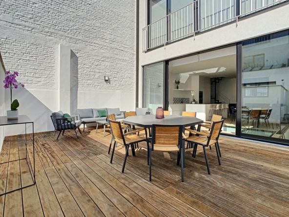 Terrasse moderne élégante avec mobilier en bois, luminothérapie et vue ouverte sur intérieur lumineux.