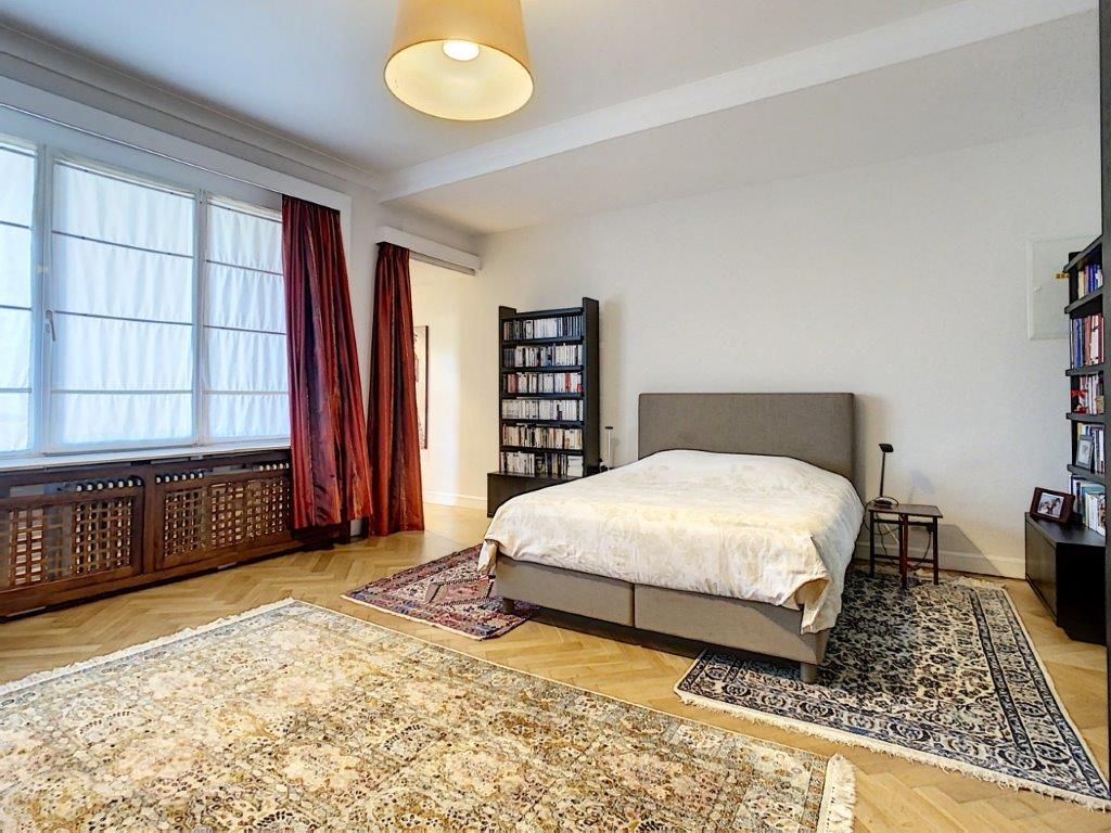 Chambre lumineuse avec grand lit blanc, bibliothèque noire, rideaux rouges et décoration élégante.