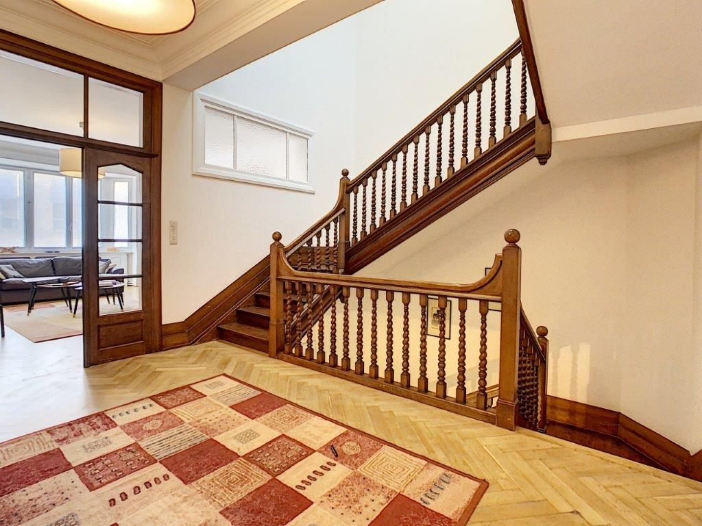 Escalier en bois sophistiqué, tapis coloré, luminosité naturelle dans une belle entrée chaleureuse.