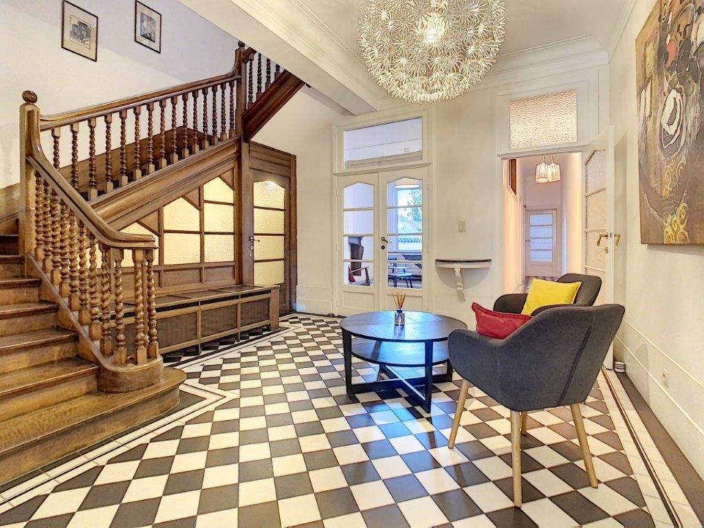 Foyer sophistiqué avec escalier en bois, chandelier, sol damier et espace moderne accueillant