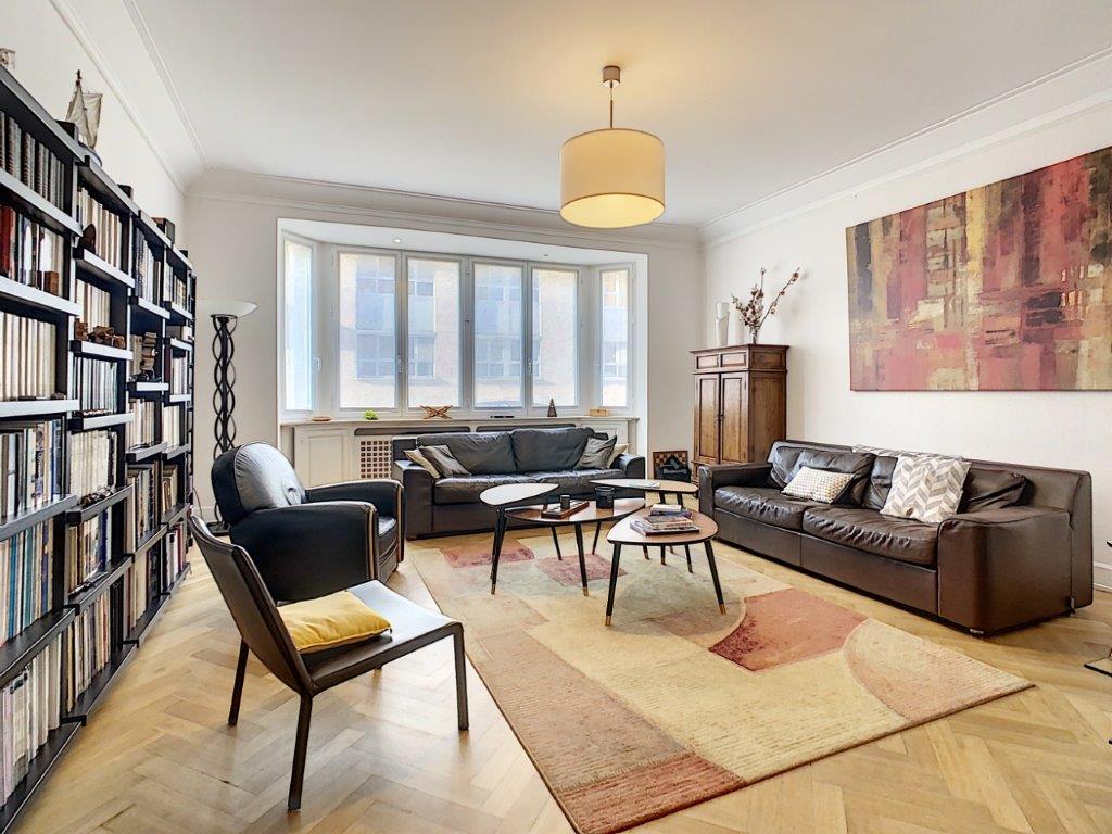 Salon moderne et cosy avec mobilier en cuir, bibliothèque, œuvre d’art abstraite et lumière naturelle.