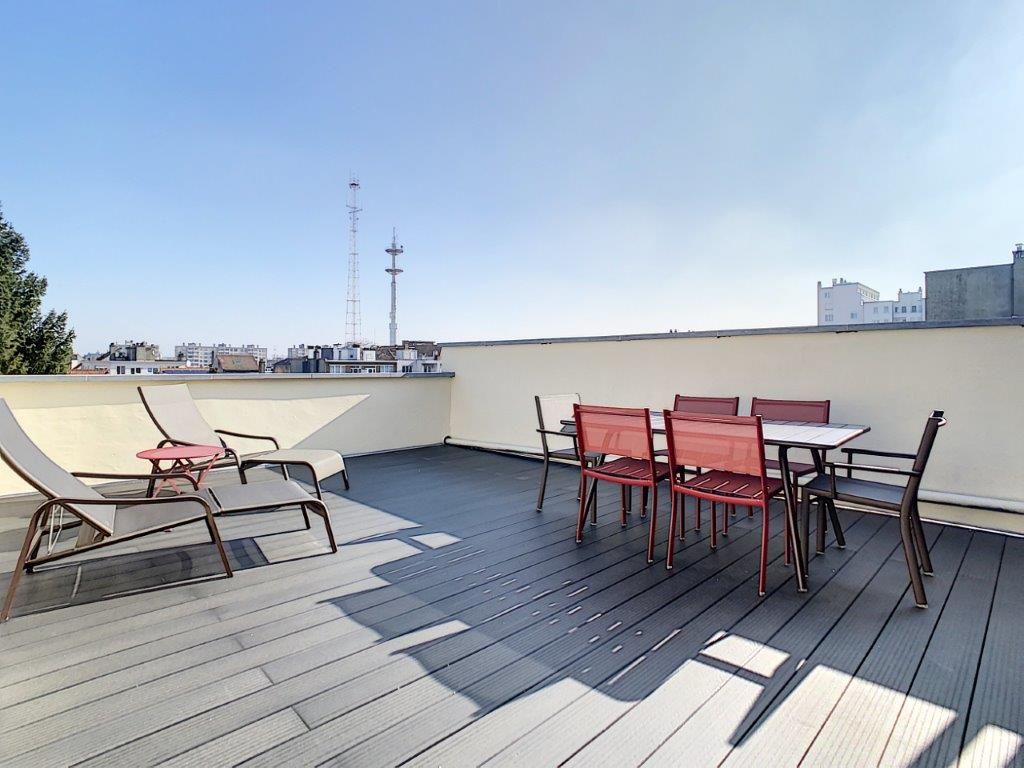 Terrasse rooftop avec mobilier rouge et vue panoramique urbaine en journée.
