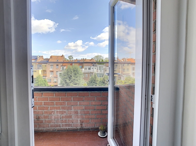 Balcon ensoleillé avec vue urbaine colorée, portes ouvertes, ciel bleu et ambiance paisible.
