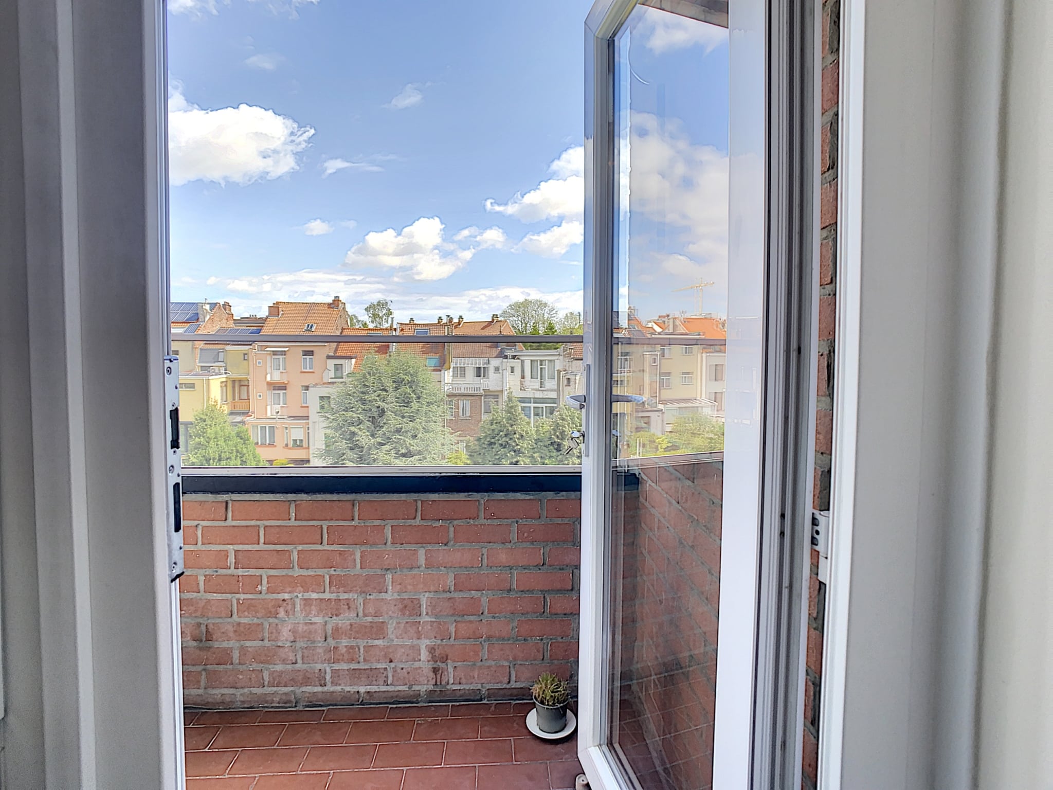 Balcon ensoleillé avec vue urbaine colorée, portes ouvertes, ciel bleu et ambiance paisible.