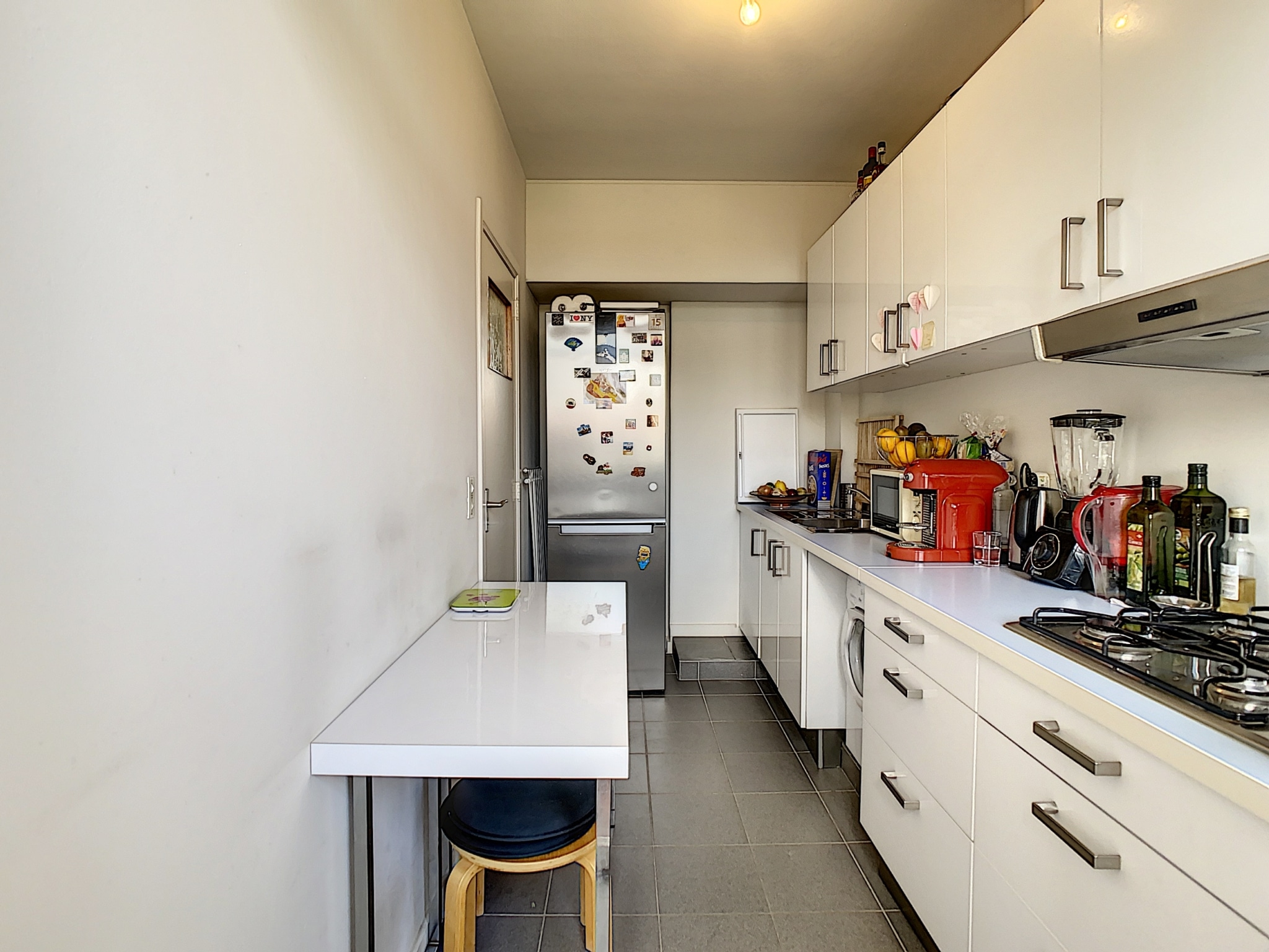 Cuisine moderne minimaliste avec électroménagers en inox, plan de travail blanc, espace repas compact.
