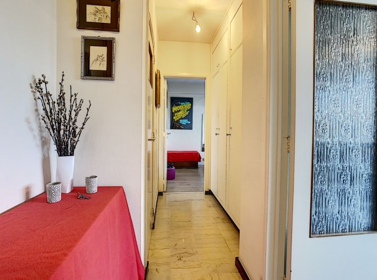 Couloir lumineux avec décorations, porte blanches, table rouge et chambre colorée au fond.