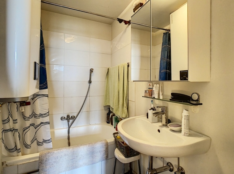 Salle de bain moderne et pratique avec lavabo rond, miroir, douche et décoration épurée.