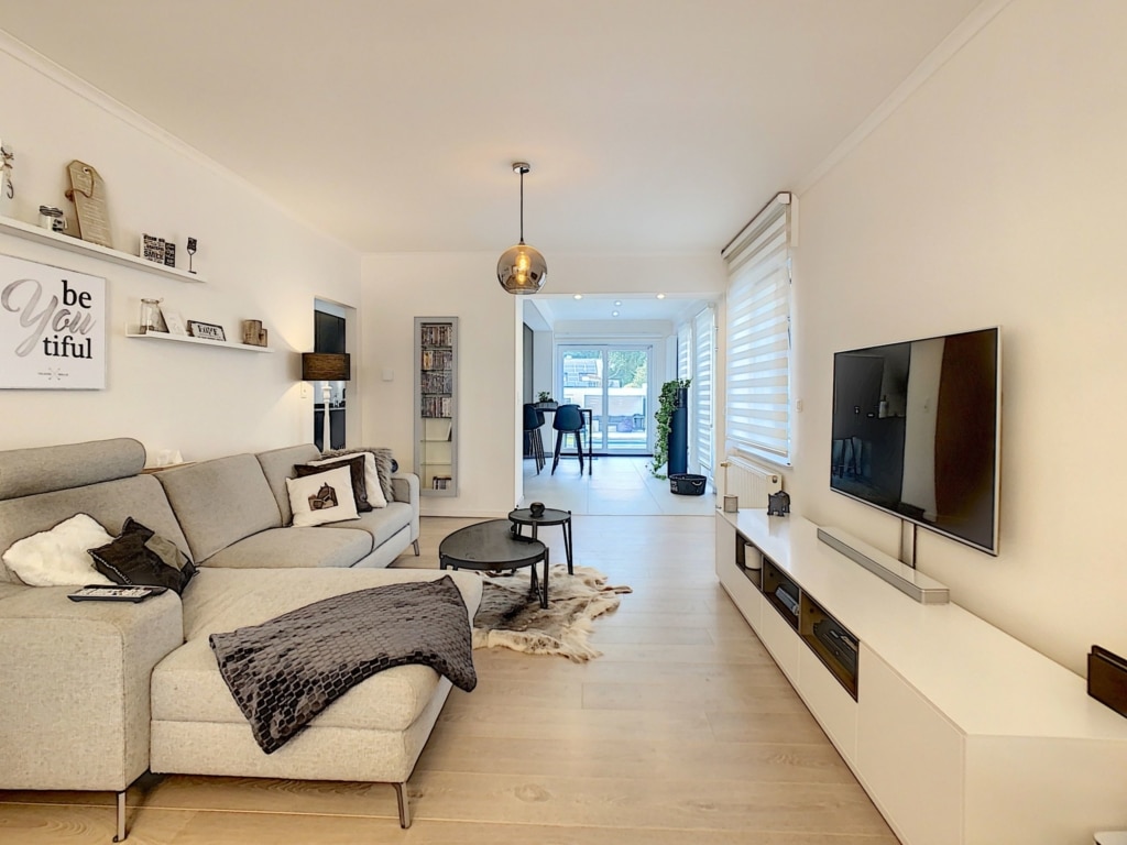 Salon moderne lumineux avec canapé gris, grande baie vitrée et décoration élégante.