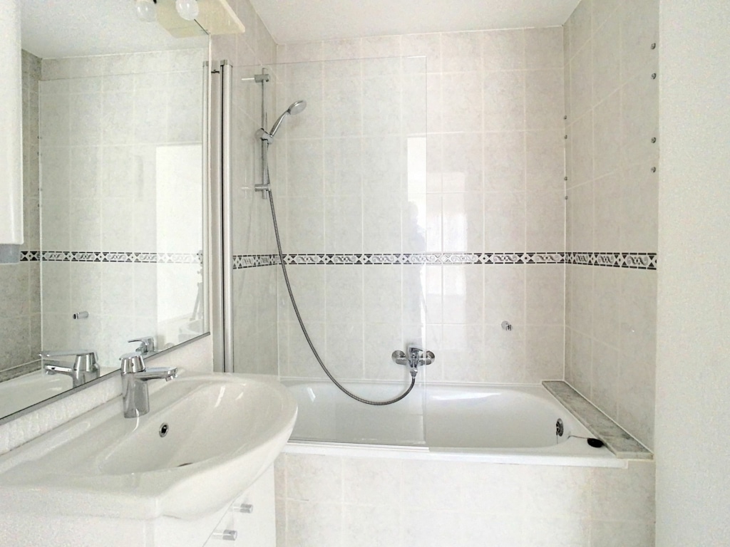Salle de bain moderne avec baignoire, douche chic, lavabo sleek, murs blancs et mosaïques élégantes.