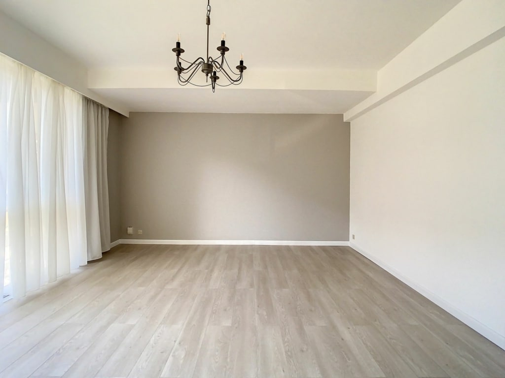 Salon lumineux épuré avec sols en bois clair, grande fenêtre et lustre élégant.