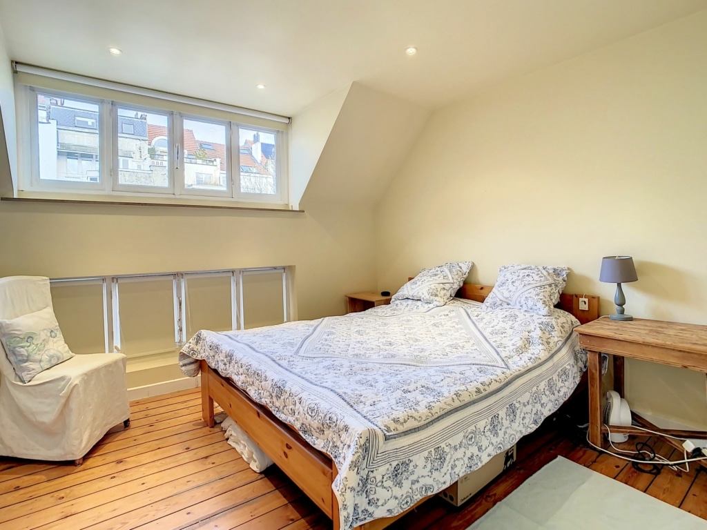 Chambre dattique lumineuse, chaleureuse, avec lit floral, chaise cozy et ambiance reposante.