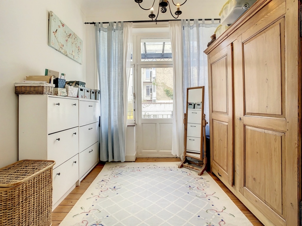 Chambre lumineuse, organisée, chaleureuse avec meubles en bois, tapis géométrique et miroir.