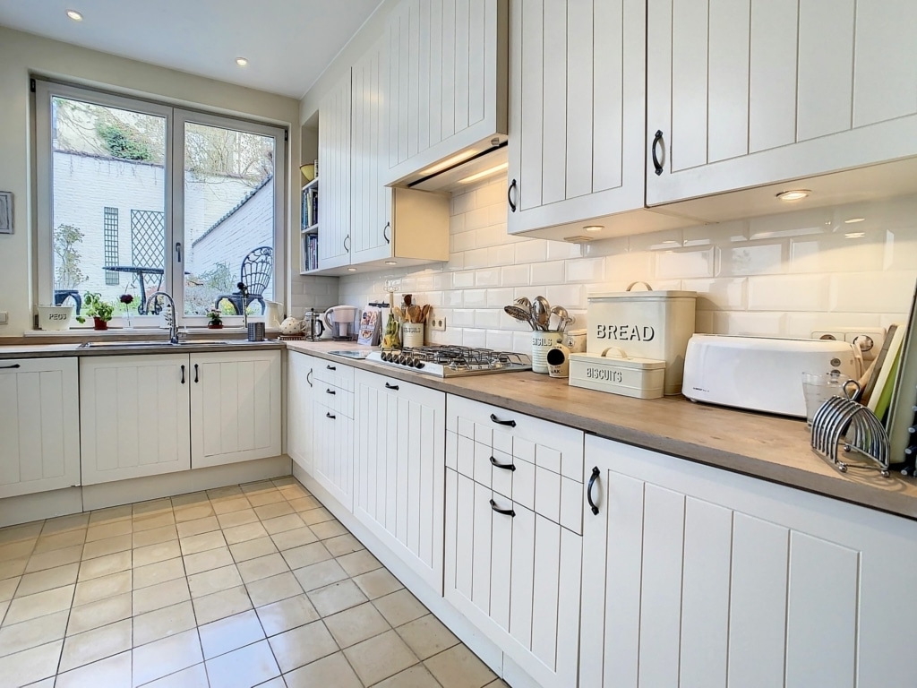 Cuisine lumineuse moderne avec meubles blancs, plan en bois et plantes d’intérieur.