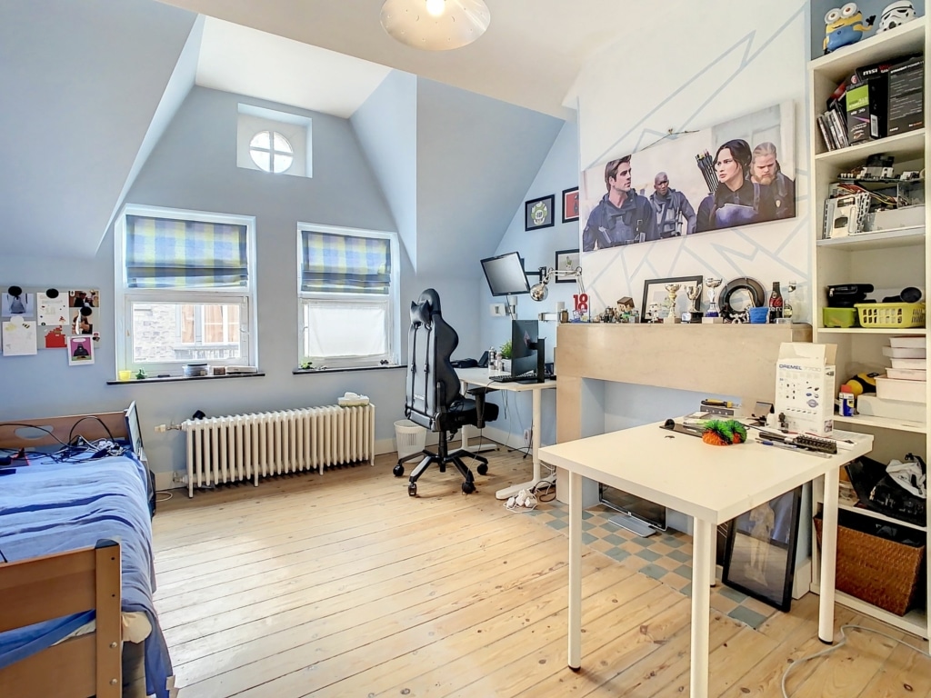 Espace cosy sous pente avec lit, bureau moderne et bibliothèque pour working et relaxation.