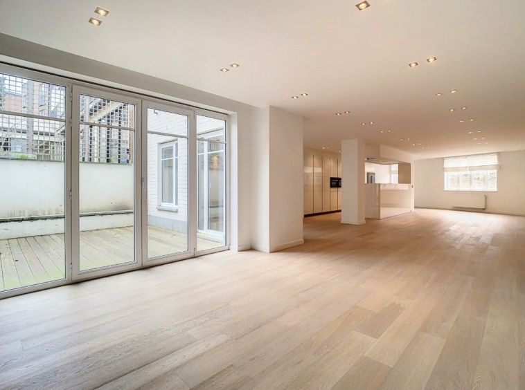 Appartement moderne lumineux avec espace ouvert, cuisine minimaliste et grande terrasse extérieure pavée.