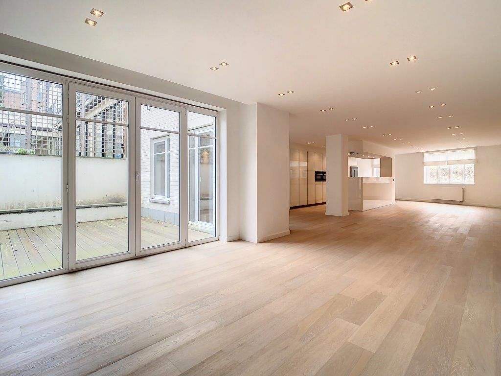Appartement moderne lumineux avec espace ouvert, cuisine minimaliste et grande terrasse extérieure pavée.