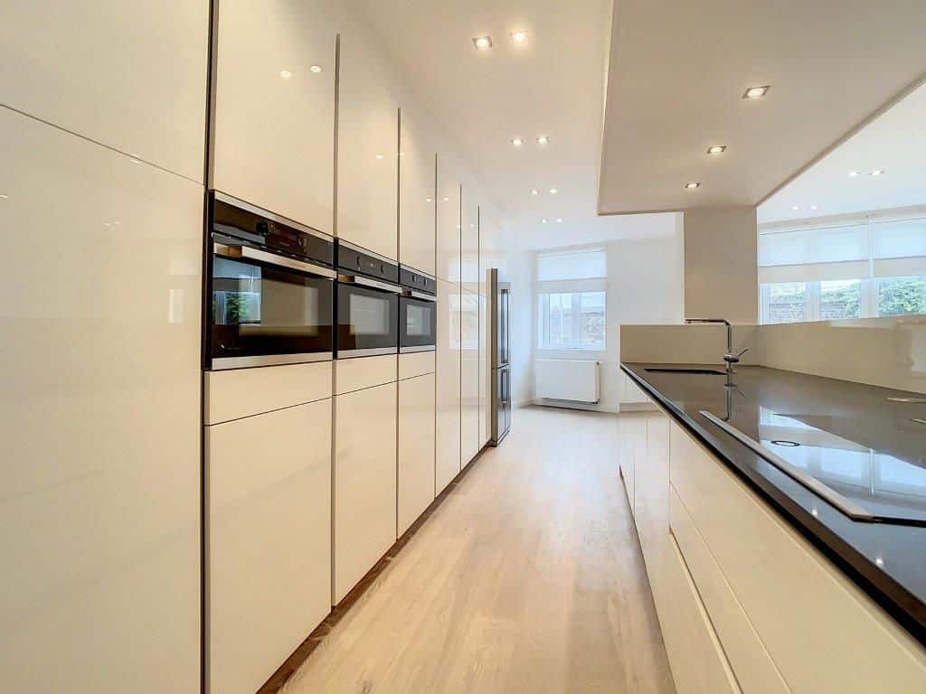 Cuisine moderne minimaliste, blanche et sombre, lumineuse, intégrée, avec sol en bois clair.