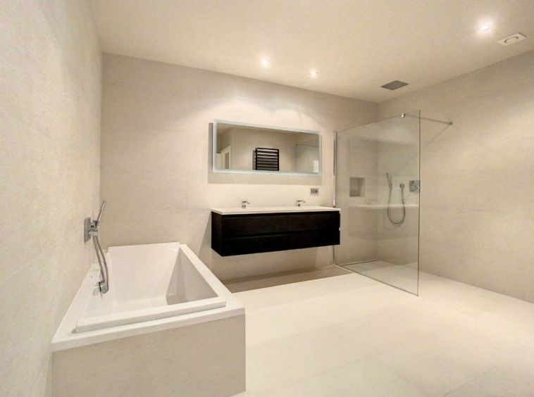 Salle de bain moderne avec baignoire blanche, douche en verre, vanity sombre et éclairage naturel.
