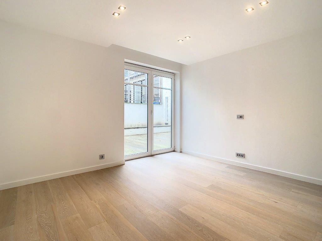 Salon lumineux minimaliste avec grande porte-fenêtre en verre, parquet clair et éclairage moderne.