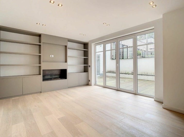 Salon lumineux avec parquet clair, étagères intégrées et grandes portes-fenêtres donnant sur le jardin.