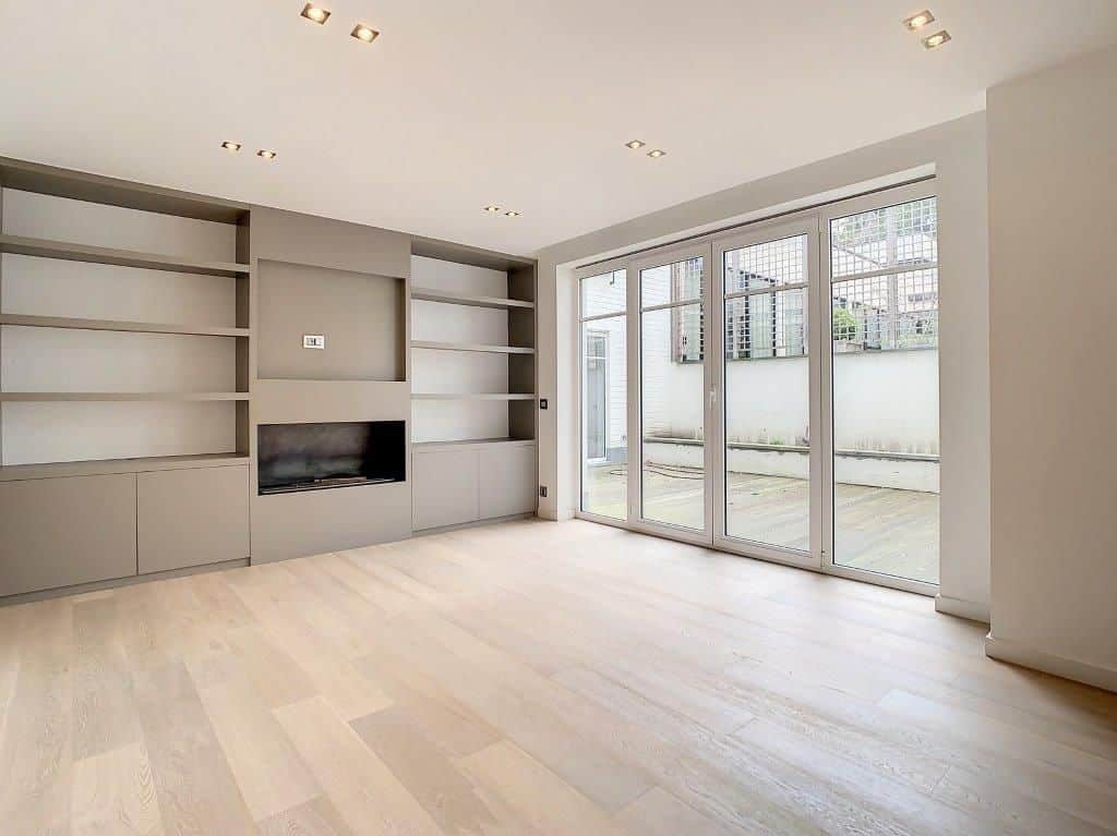 Salon lumineux avec parquet clair, étagères intégrées et grandes portes-fenêtres donnant sur le jardin.
