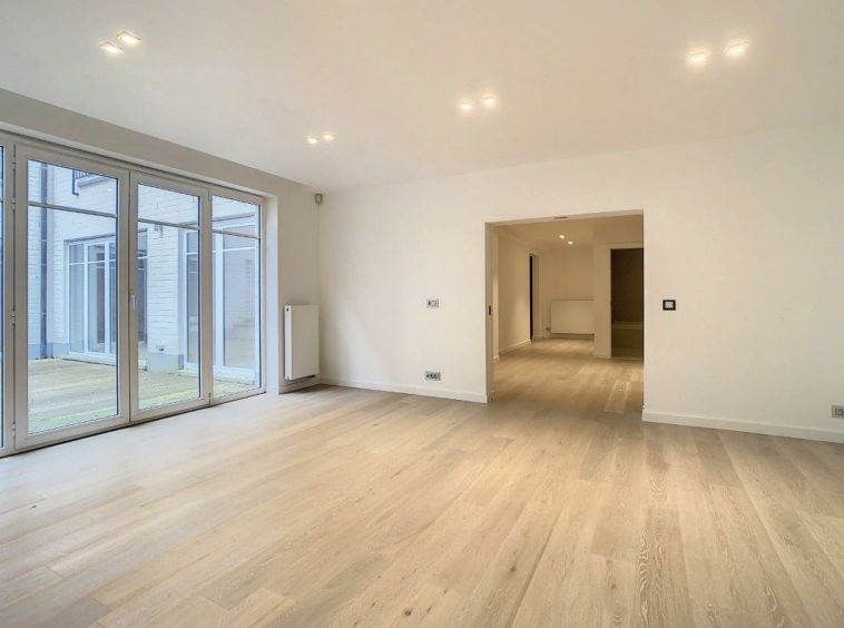 Salon lumineux avec grandes portes vitrées, parquet clair, espace ouvert et ambiance moderne.