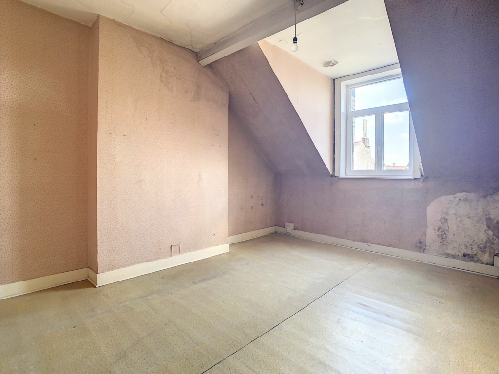 Chambre attique lumineuse à rénover, charme rustique, murs roses usés, grande fenêtre, parquet ancien.