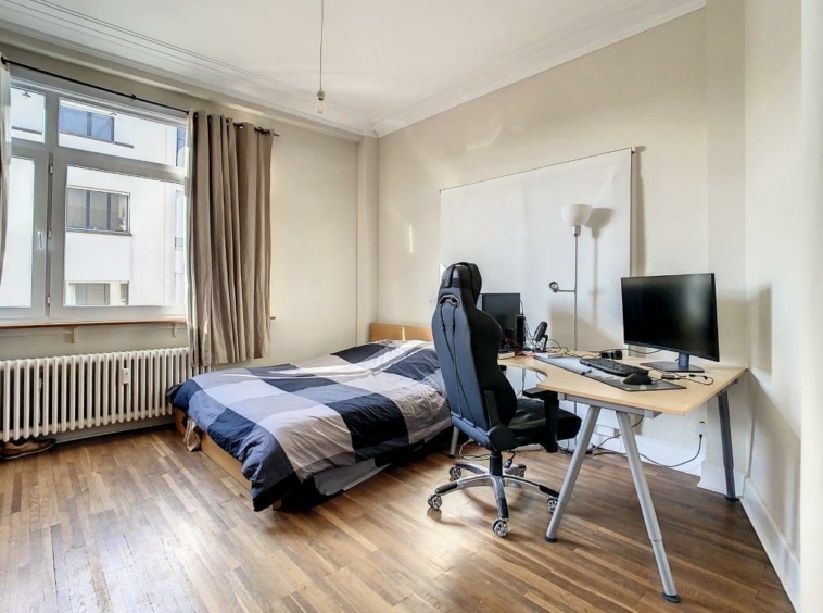 Chambre cosy avec lit, bureau et grande fenêtre pour lumière naturelle et confort.