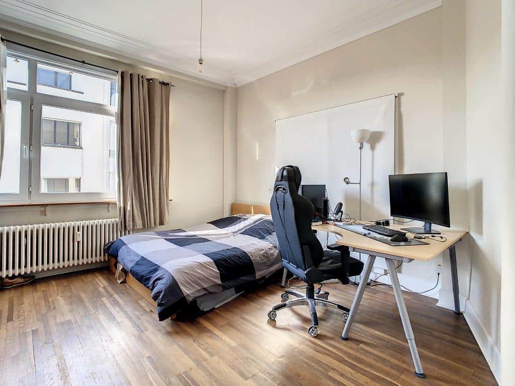 Chambre cosy avec lit, bureau et grande fenêtre pour lumière naturelle et confort.