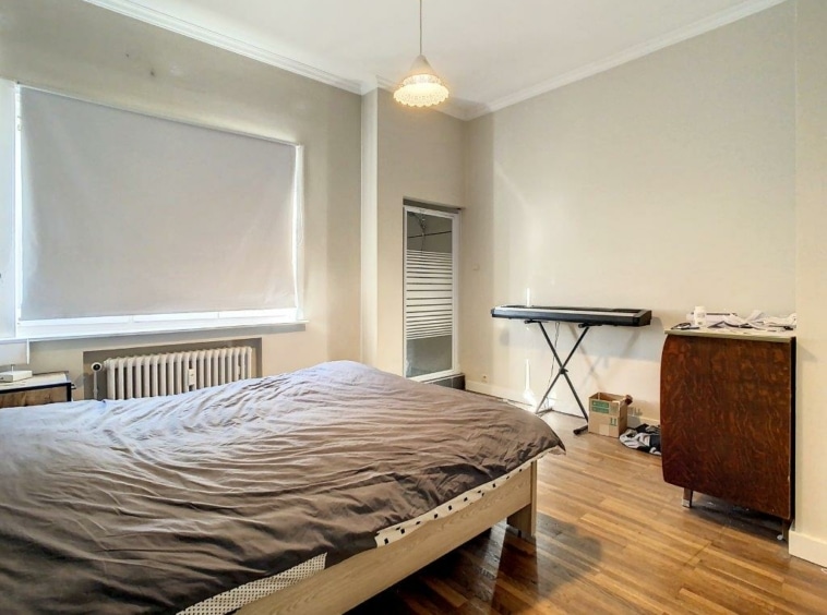 Chambre minimaliste chaleureuse avec lit gris, miroir, clavier, meuble en bois et ambiance apaisante.