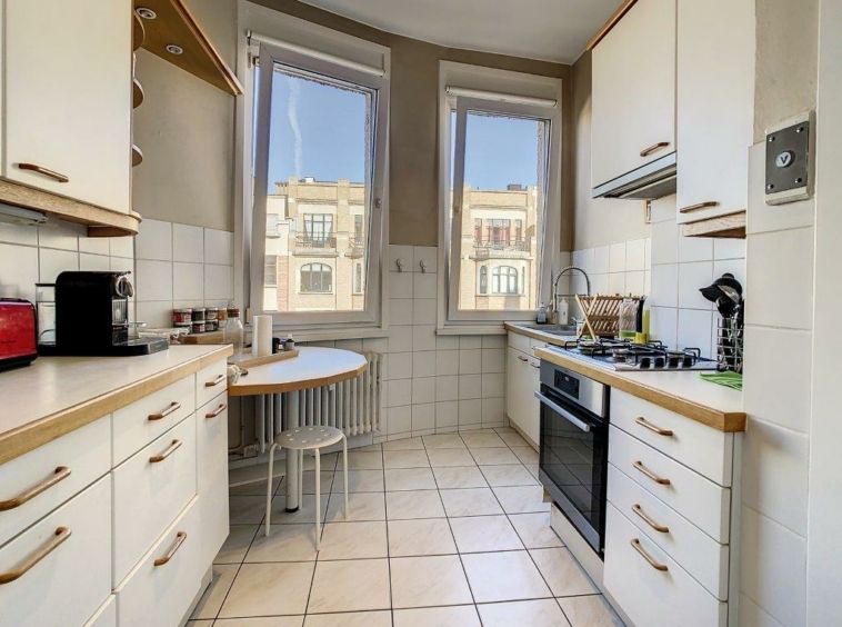 Cuisine moderne lumineuse avec mobilier blanc, plan en bois, grande lumière naturelle, et espace convivial.