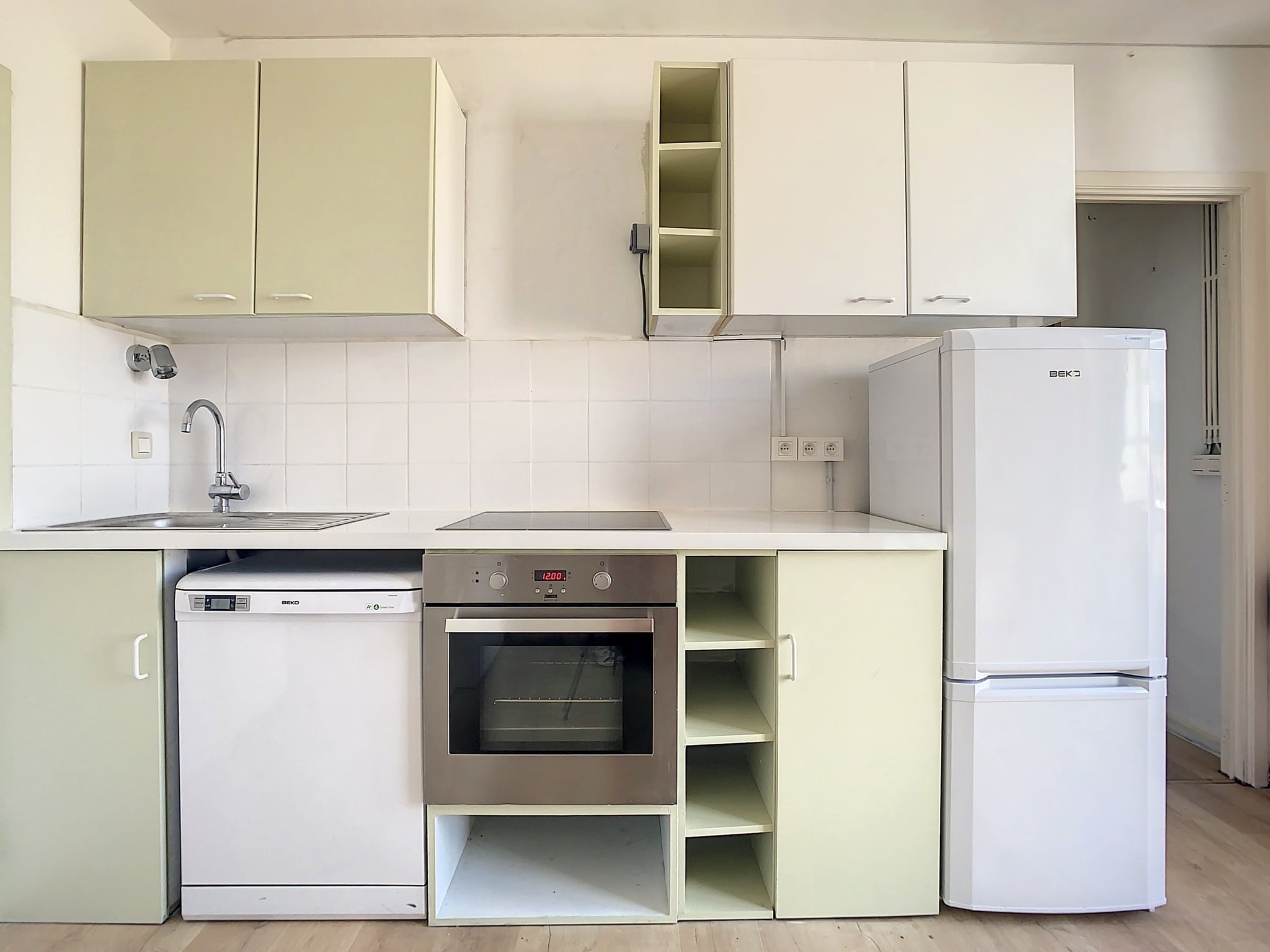 Cuisine moderne minimaliste avec meubles jaunes, plan inox, évier sous fenêtre et sol en bois clair.
