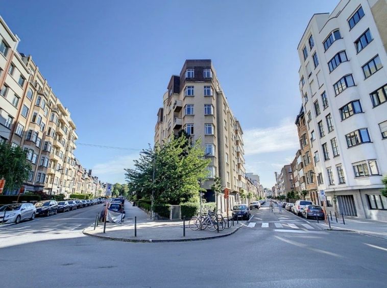 Quartier moderne with greenery, bike racks, and busy streets under sunny blue sky.