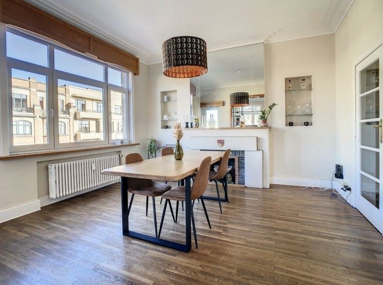 Salle à manger moderne lumineuse avec table en bois, chaises élégantes, cheminée et décor végétal.