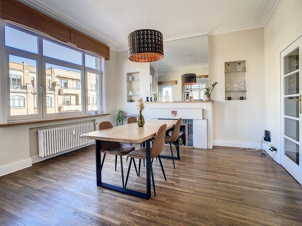 Salle à manger moderne lumineuse avec table en bois, chaises élégantes, cheminée et décor végétal.