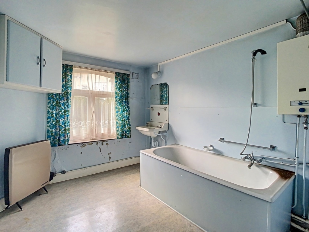 Salle de bain vintage simple avec baignoire, lavabo, rangements et fenêtre à rideaux bleus.