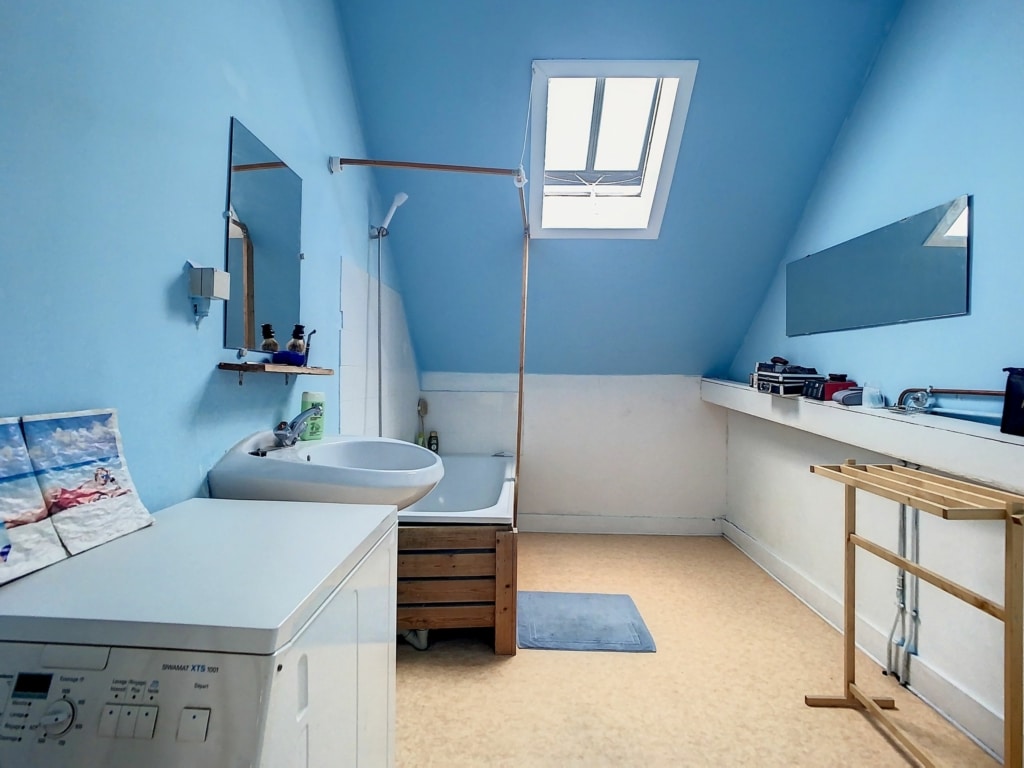 Salle de bain mansardée lumineuse avec baignoire en bois, lave-linge intégré et skylight.